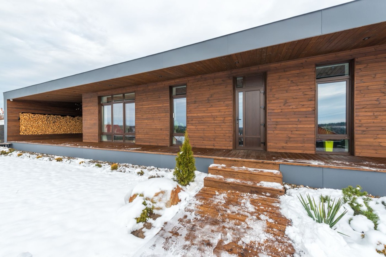 Maison en bois sous la neige avec sa réserve de bûches pour l'hiver